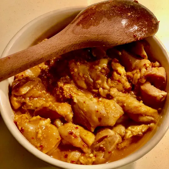 chicken thighs marinating in a bowl with wooden spoon on top